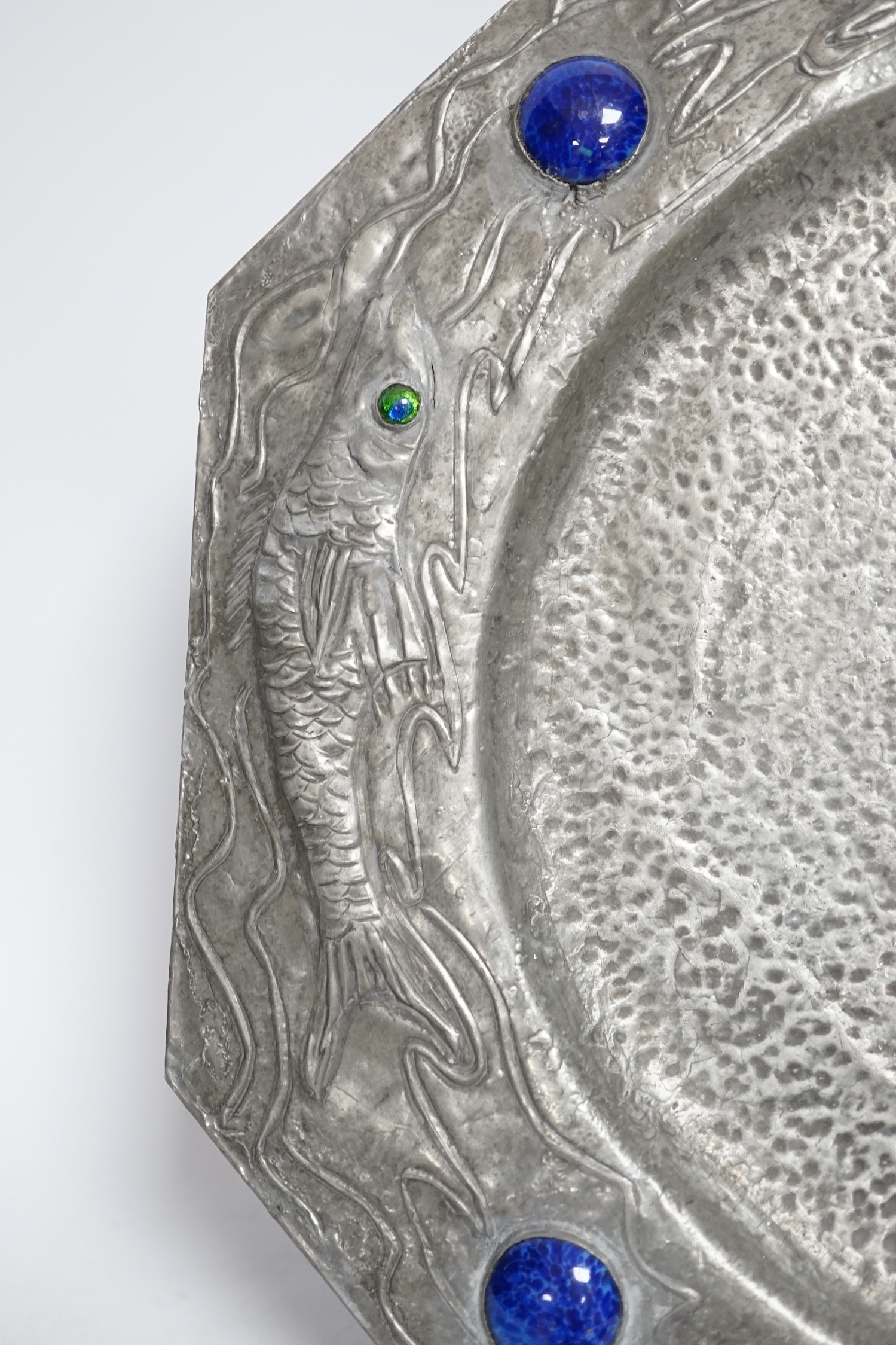 An Arts and Crafts style pewter fish plate with ceramic insets and glass eyes together with a pottery armorial charger, pewter charger 35cm wide